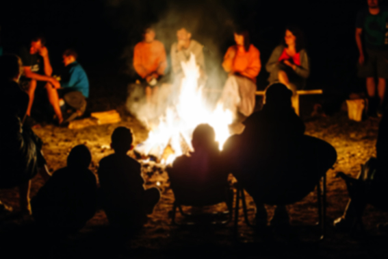 Blurred People sit at night round a bright bonfire
