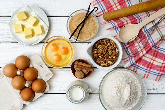 Baking cake in rural kitchen - dough recipe ingredients (eggs, flour, milk, butter, sugar) on white wooden table from above.